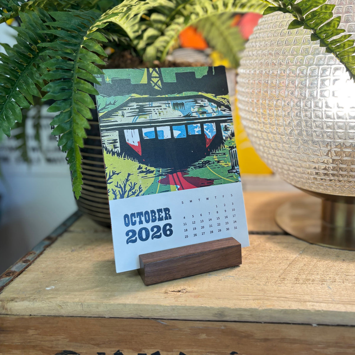 Calendar showing October 2026 on a wooden stand with decorative elements in the background.